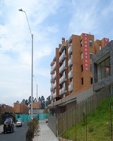 Imagen con sendero peatonal en el centro, a los lados zonas verdes amplias y al final edificios residenciales. 