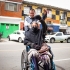 Mujer adulta usuaria de silla de ruedas acompañada de un hombre joven, ambos con el brazo arriba como símbolo de victoria