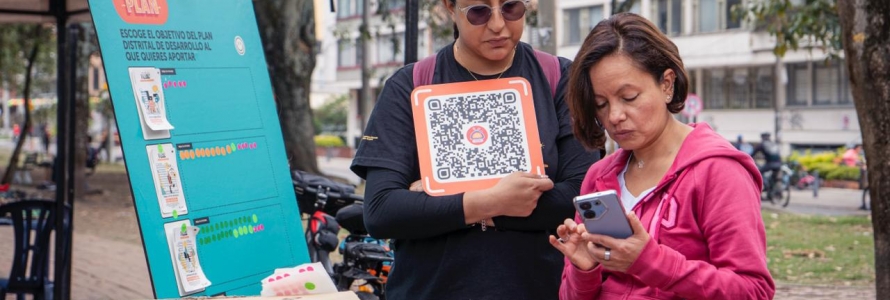 Ciudadana con su celular escaneando código QR de chatico, junto a servidora de la Secretaría Distrital de Planeación.