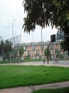 Imagen que contiene en su parte frontal una zona verde con caminos peatonales y un parque con canchas de juegos, al fondo se encuentra un conjunto residencial de apartamentos. 